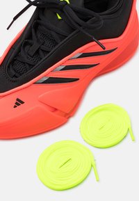 Fekete szövet felsőrésszel rendelkező sportcipő, élénk narancssárga gumi talppal és fényvisszaverő ezüst csíkokkal. Két neon zöld cipőfűzőt tartalmaz.