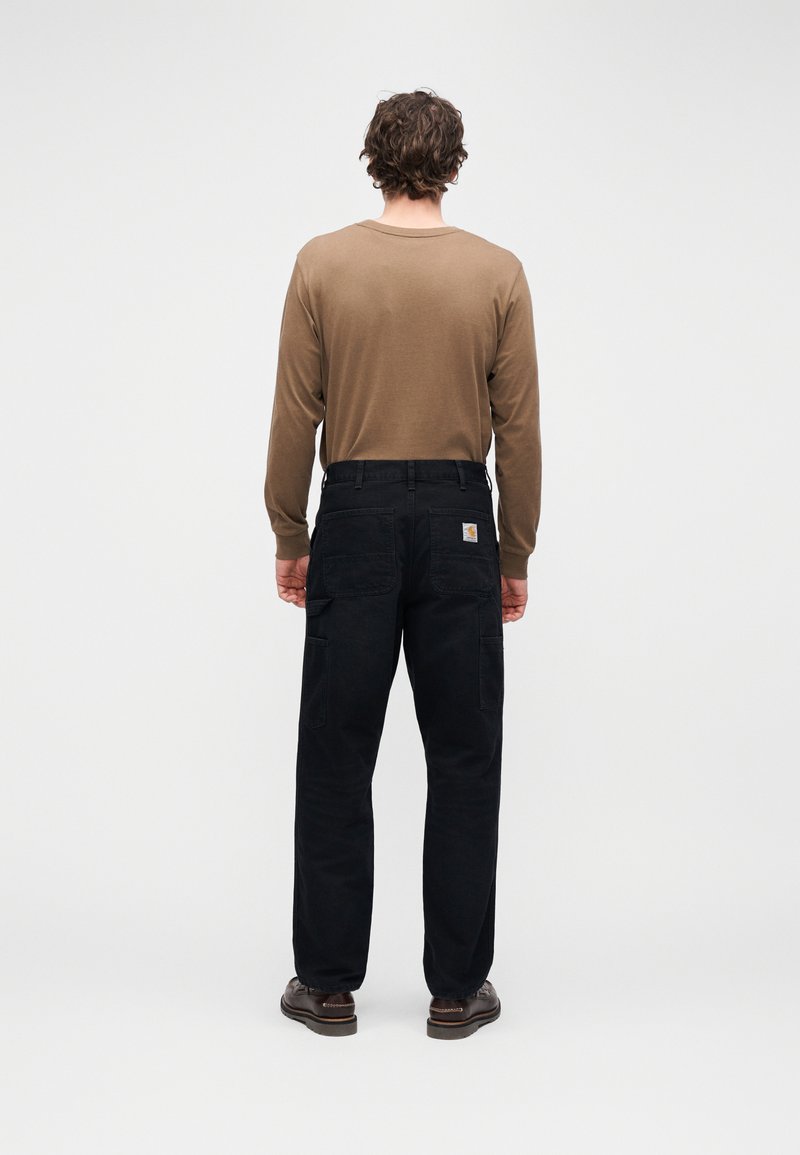 Camicia marrone a maniche lunghe abbinata a pantaloni cargo neri con tasche frontali e posteriori, realizzati in tessuto resistente, indossata con scarpe marroni.