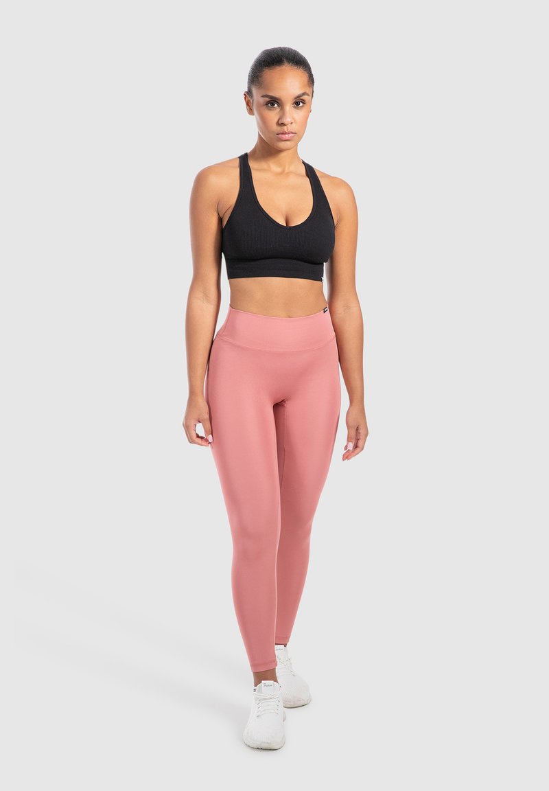Reggiseno sportivo nero a coste e leggings rosa a vita alta, realizzati in tessuto elasticizzato, abbinati a scarpe da ginnastica bianche. Design semplice, silhouette aderente.