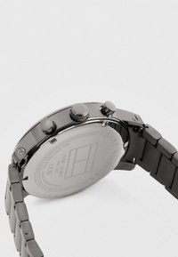 Orologio da polso in metallo con bracciale a maglie, cassa rotonda sul retro incisa con dettagli del marchio e della resistenza all'acqua, e tre pulsanti di controllo sul lato.