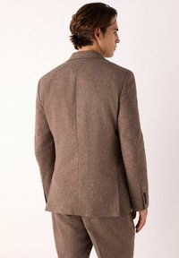 Blazer marrón texturizado con cierre de dos botones, solapas de pico y abertura trasera, con un ajuste entallado y un brillo sutil.