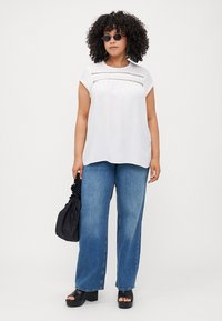 White top with short sleeves and lace detailing, paired with loose blue jeans, black platform sandals, and a black bag.