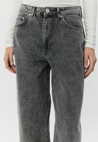 Temno sivi jeans hlače z visokim pasom, petimi žepi in gumbom za zapiranje. Teksturiran material z obrabljenim videzom, nekoliko ohlapen kroj.