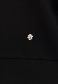 Petit bouton métallique rond avec un symbole de cœur et le texte « Key Largo » sur un fond de tissu noir.