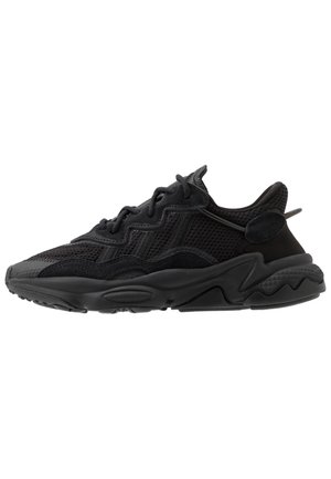 Svart atletisk sneaker laget av mesh og semsket skinn, med teksturert overflate, skulpturert såle og kontrasterende snører. Slank silhuett og polstret krage.