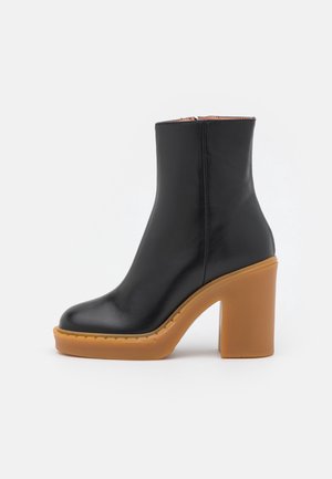 Bottine noire en cuir avec semelle plateforme épaisse couleur fauve et talon haut épais, fermeture éclair latérale et finition lisse.