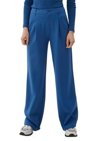 Breda byxor i ljusblått tyg, med knappstängning och framfåror. Tillsammans med grå och vita sneakers.