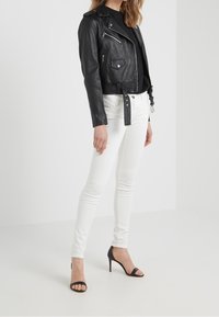 Svart lädermotorcykeljacka med silvriga dragkedjor och knappar, parat med åtsittande vita jeans och svarta strappy högklackade skor.