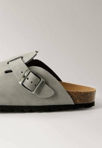 Gray suede sandal featuring a wide strap with a silver metal buckle, cork footbed, and textured black rubber outsole.