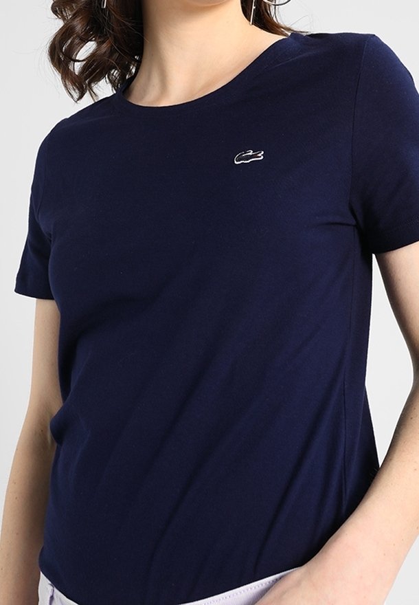 Námořnická modrá tričko s krátkým rukávem vyrobené z bavlny, s malým bílým logem Lacoste na hrudi a klasickým kulatým výstřihem.