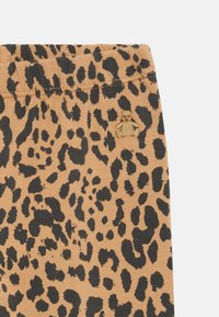 Leopárdmintás leggings puha anyagból, bézs hátterével, fekete pöttyökkel és egy kis hímzett medve logóval a derékrészen.