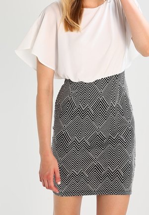 Kvinde iført en kortærmet hvid bluse og et højtaljet sort-hvidt nederdel med geometrisk mønster.