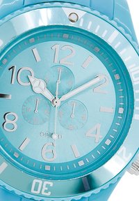 Montre analogique turquoise avec une finition brillante, grands chiffres argentés, sous-cadrans et un bracelet en silicone texturé. Notable pour sa couleur vive.