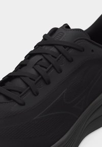 Μαύρο αθλητικό παπούτσι με υφασμένο επάνω μέρος, μαύρα κορδόνια δεμένα στα πόδια, και παχύ πέλμα με διακριτικό λογότυπο της μάρκας στην πλευρά.