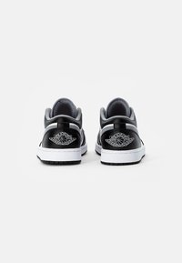 Zapatillas de cuero negras y grises con suelas blancas, que cuentan con un logotipo circular y detalles de costura en el talón. Diseño de textura suave.