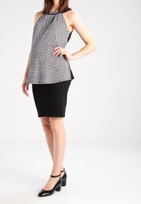 Top halter in bianco e nero con motivo houndstooth, con fronte drappeggiato, abbinato a una gonna a tubino nera attillata; il modello indossa scarpe nere con tacco a blocco.