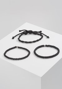 Tre svarte armbånd: en fletteledd stil, et rundt perledesign og en flat rektangulær perlestil, alle med teksturerte, glatte overflater.