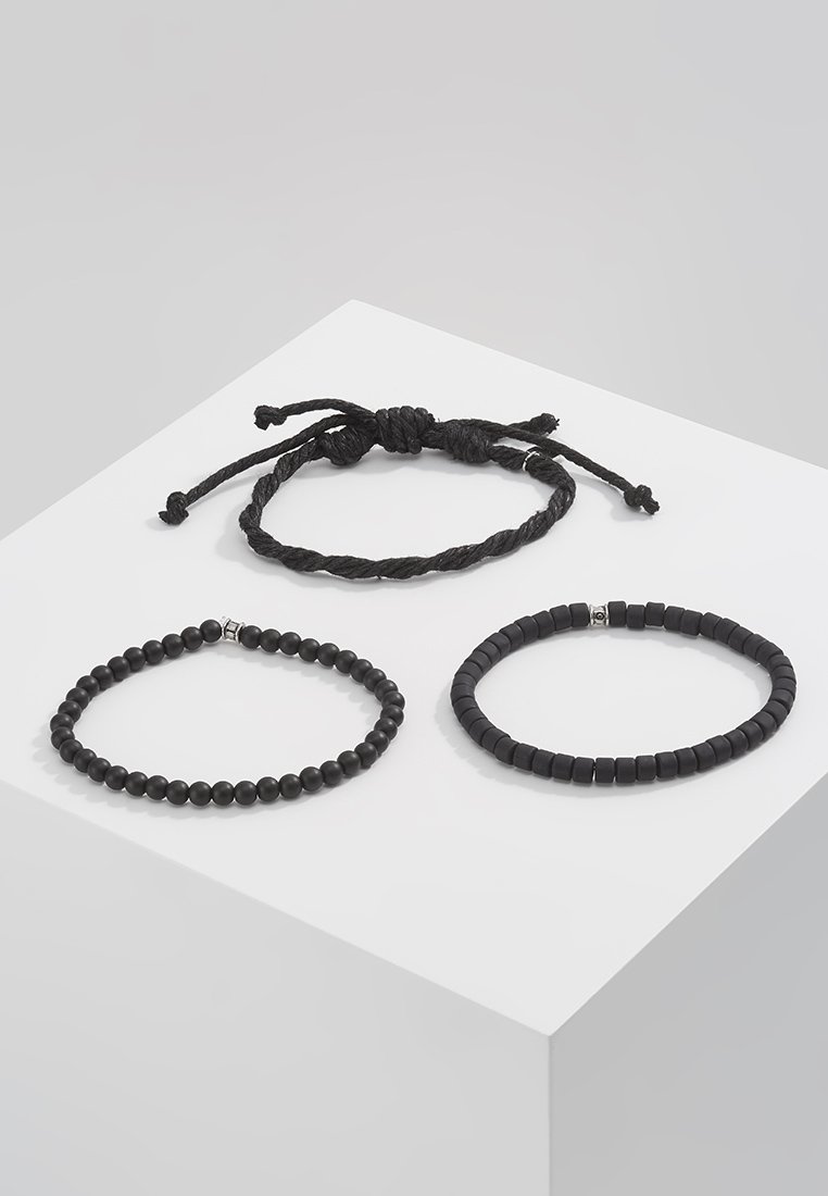 Tre svarte armbånd: en fletteledd stil, et rundt perledesign og en flat rektangulær perlestil, alle med teksturerte, glatte overflater.