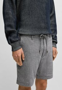 Harmaat pellavashortsit, joissa on teksturoitu pinta, kiristysnauha vyötäröllä, etutaskut ja rento istuvuus. Yhdistetty tummaraitaiseen neulepaitaan.