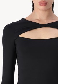 Black bodysuit featuring long sleeves, a cross-over design at the neckline, and a cut-out detail under the bust. Smooth fabric texture.