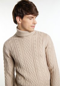 Beżowy sweter z golfem, pleciony, z wzorami warkoczowymi i prążkowanymi detalami. Miękka faktura z różnymi grubościami w wzornictwie.