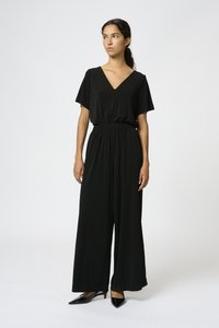 Svart jumpsuit med V-ringning, korta ärmar och vida ben. Elastisk midja för komfort. Modellen bär svarta pumps med spetsig tå.