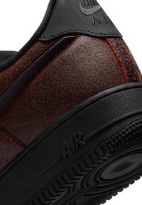 Zbliżenie na piętę teksturowanego buta sportowego w ciemnoczerwonym i czarnym kolorze z czarną gumową podeszwą, z napisem "AIR" i logo Nike na górnej części.