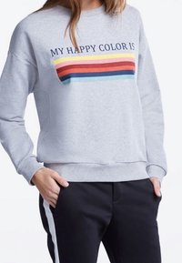 Sudadera gris con el texto "MI COLOR FELIZ ES", presenta rayas horizontales multicolores en rojo, amarillo, azul y verde. Ajuste casual.