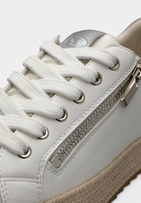 Λευκό δερμάτινο αθλητικό παπούτσι σε κοντινή λήψη με υφασμένα κορδόνια, ασημένιες μεταλλικές λεπτομέρειες και διακοσμητικό φερμουάρ. Φυσικός ενδιάμεσος πάτος σε στυλ γιούτας.