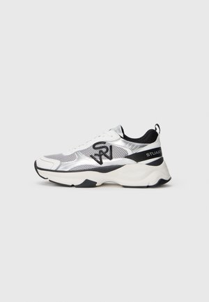 Sneaker atletica argento e bianca con materiale in rete e sintetico, collo imbottito, dettagli neri e suola spessa. Dettaglio del logo nero sul lato.