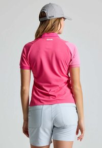 Lichtroze polo met korte mouwen, raglanontwerp en logo op de kraag. Gecombineerd met lichtgrijze shorts met achterzakken.