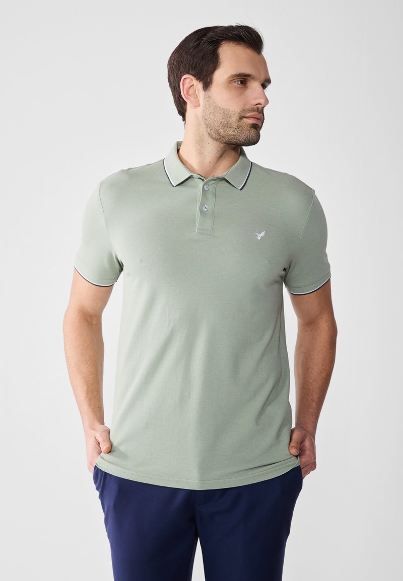 Polo de manga corta en verde apagado, con un cuello con borde en contraste azul marino, tapeta de tres botones y logo bordado en el pecho.