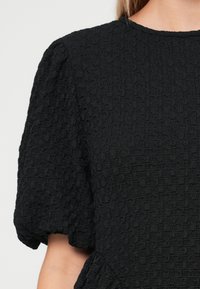 Vestido preto texturizado com mangas bufantes curtas e decote redondo, apresentando um tecido franzido e detalhamento plissado na cintura.