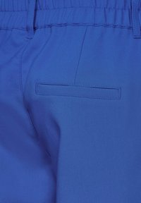 Blå tygbyxor med elastisk midja, med en bakficka och slät textur, framhävd av fina sömnadsdetaljer.