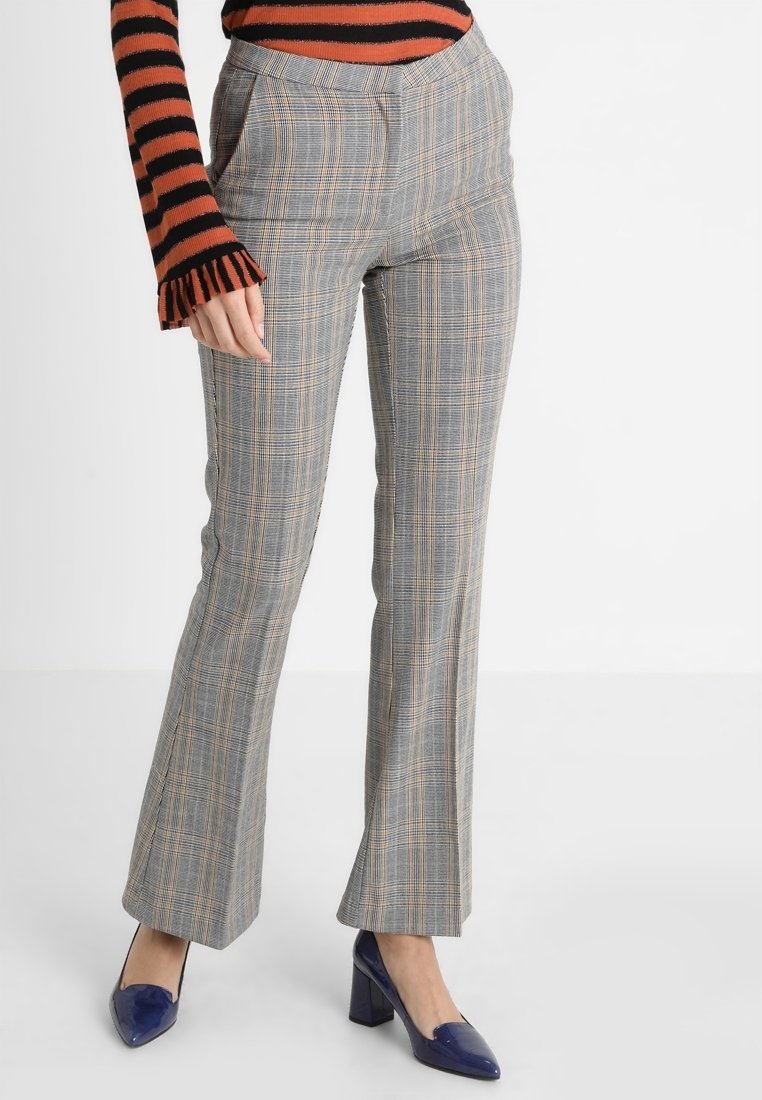 Grå rutiga byxor med en utsvängd bendesign, med ett rutmönster i ljusbruna accenter. Bärs med en svart och orange randig topp.