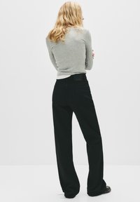 Jean noir large à taille haute, assorti d'un haut gris ajusté à manches longues. La tenue présente une étiquette discrète au dos et des lignes épurées.