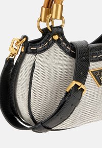 Black and white handbag with a structured shape, textured fabric, gold hardware, and a woven pattern. Features a detachable strap and logo accent.