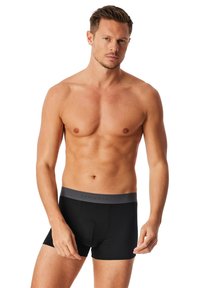 Schwarze Boxershorts mit einem grauen elastischen Bund, der das „SCHIESSER“-Logo zeigt. Der Stoff wirkt glatt und dehnbar, mit einem taillierten Design.