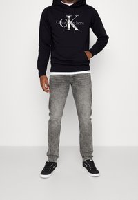 Felpa con cappuccio navy con logo "Calvin Klein Jeans", abbinata a jeans grigio chiaro sbiaditi e sneakers nere con suola bianca.