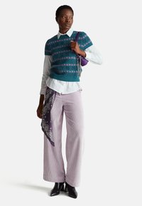 Pletený tyrkysový svetr s růžovým vzorem přes bílou košili, doplněný světle fialovými širokými kordurovými kalhotami. Černé kozačky na podpatku a fialová kabelka.