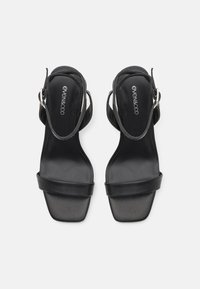 Sorte slingback sandaler med firkantet tå, glatt lærmateriale og en bred stropp over fronten. Justerbar ankelspenne.