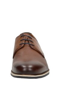 Chaussure en cuir marron à lacets avec une tige texturée, un bout lisse et des coutures blanches contrastées le long de la semelle. Forme arrondie, design minimaliste.