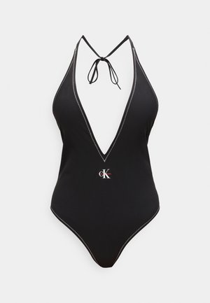 Musta halterneck-uimallinen, jossa syvä V-pääntie, valkoinen ompelu ja pieni Calvin Klein -logo keskellä edessä.