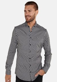 Schwarz-weiße Button-up-Bluse mit einem Rautenmuster, langen Ärmeln und klassischem Kragen. Der Stoff wirkt glatt mit einem subtilen Glanz.