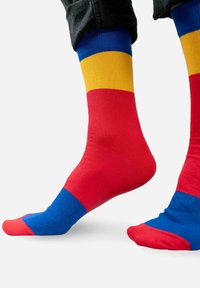 Kolorowe skarpetki z poziomymi paskami w kolorach czerwonym, żółtym i niebieskim, wykonane z miękkiej tkaniny, z kontrastującymi częściami na palcach i pięcie.