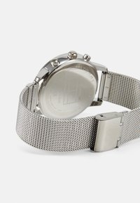 Silbernes Netzarmbanduhr mit einem Gehäuse aus Edelstahl, ausgestattet mit einem glatten Rückenteil und zwei Druckknöpfen. Schlankes, minimales Design durchgehend.