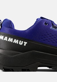 Blauer und schwarzer Wanderschuh mit strukturierter Sohle und weißem "MAMMUT"-Logo auf der schwarzen Zwischensohle, seitlich gezeigt.