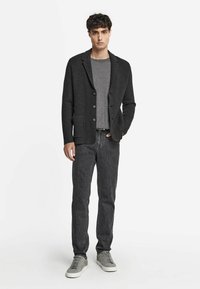 Dunkelgrauer gestrickter Blazer mit zwei Fronttaschen, Knopfverschluss und Rundhalsausschnitt unterm grauen Hemd. Kombiniert mit dunkler Jeans und grauen Sneakers.
