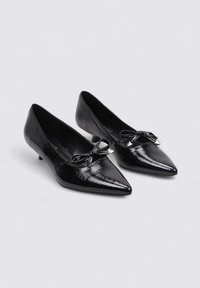 Escarpins en cuir verni noir avec un design à bout pointu, petit talon et un nœud décoratif avec des accents métalliques à l'avant.