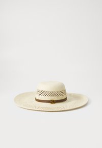 Breiter Strohhut mit einem gewebten Muster, versehen mit einem braunen Band und einem goldenen Emblemakzent. Hellbeige Farbe und strukturierte Oberfläche.